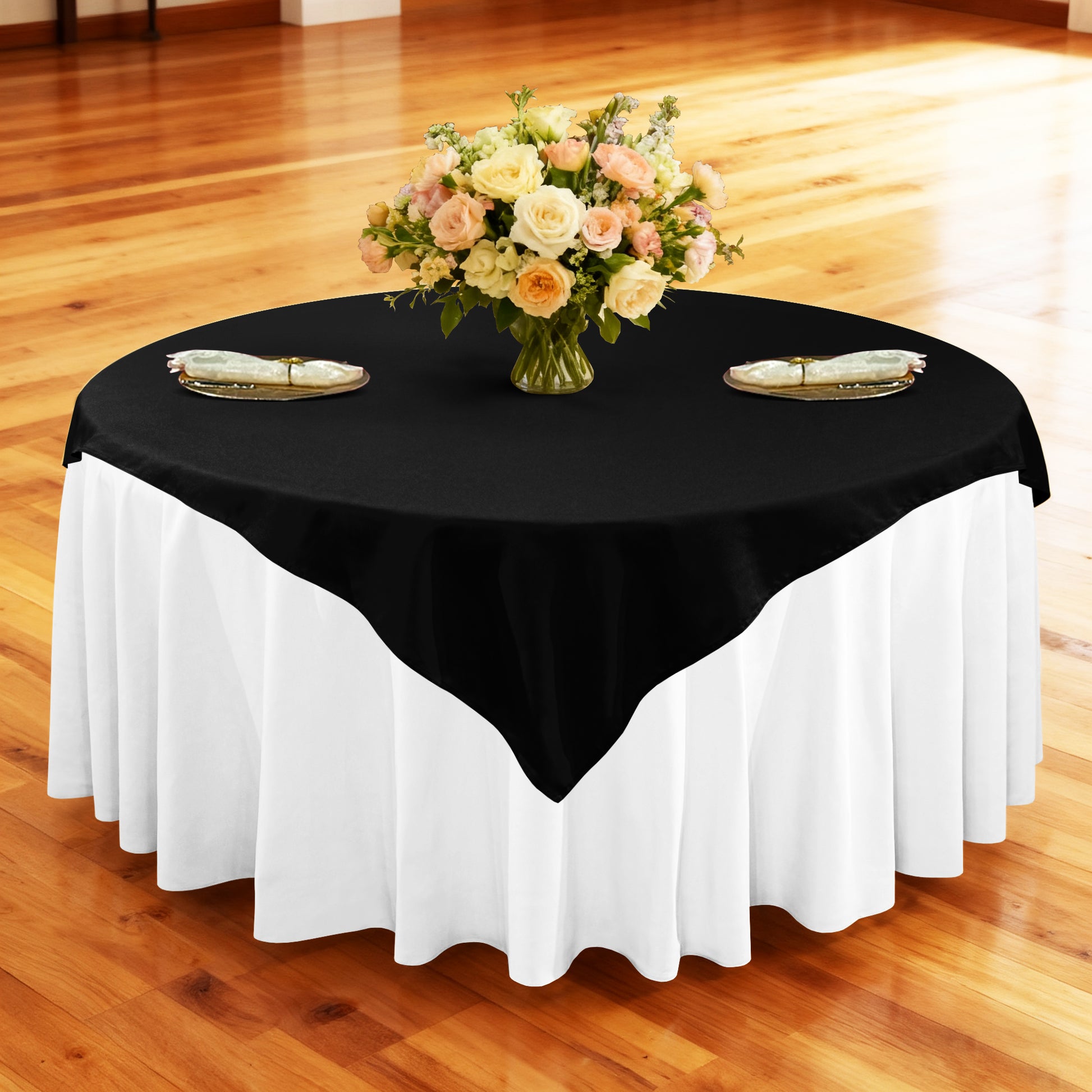Premium Spun Polyester Square 90"x90" Overlay/Tablecloth Black table setting with floral centerpiece, gold charger plates, ivory napkins ontop a white tablecloth 