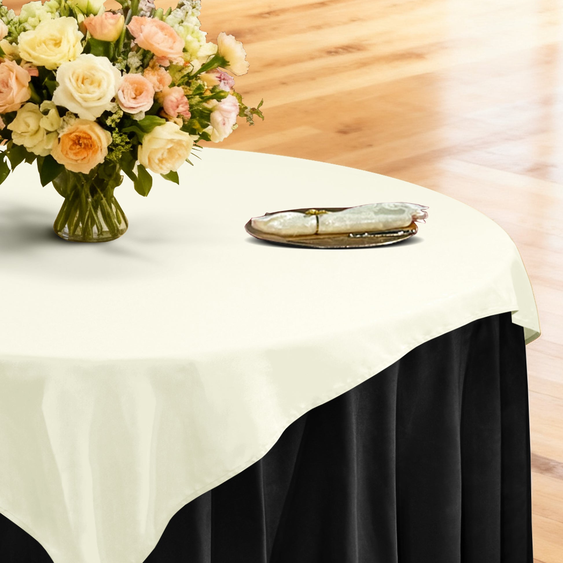 Premium Spun Polyester Square 90x90 Overlay Tablecloth Ivory table setting with floral centerpiece, gold charger plate, ivory napkin ontop a black tablecloth 