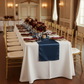 Satin Table Runner - Navy Blue on top of white tablecloth with burgundy napkin, gold charger plate, and gold chiavari chairs