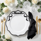 Scalloped Bow Acrylic Charger Plate Black setting with a black napkin, gold utensils, and white roses