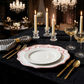 Scalloped Bow Acrylic Charger Plate Pink on top a black tablecloth with striped napkins with a gold napkin ring, gold utensils and champagne glasses