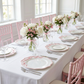 Scalloped Bow Acrylic Charger Plate Pink on top a white tablecloth, with silver silverware, floral centerpieces and pink chiavari chairs