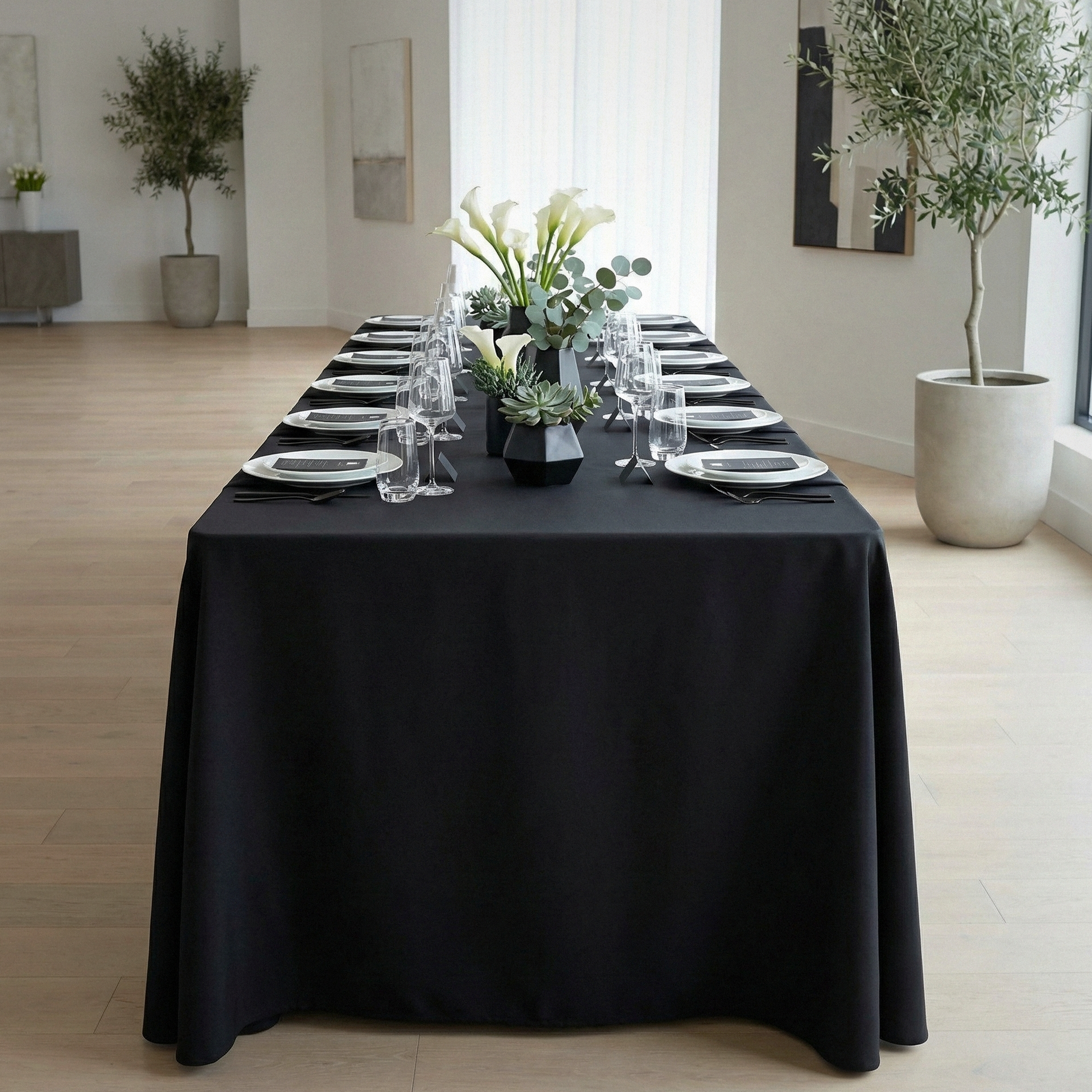 dinner setup using the Scuba King 108"x156" Rectangular Tablecloth Black paired with wine glasses, white charger plates and sinmple florals