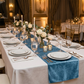 wedding rectangular tables with the Velvet Table Runner Steele Bllue with white dinner plates, silver flatware, on top a white polyester spun tablecloth