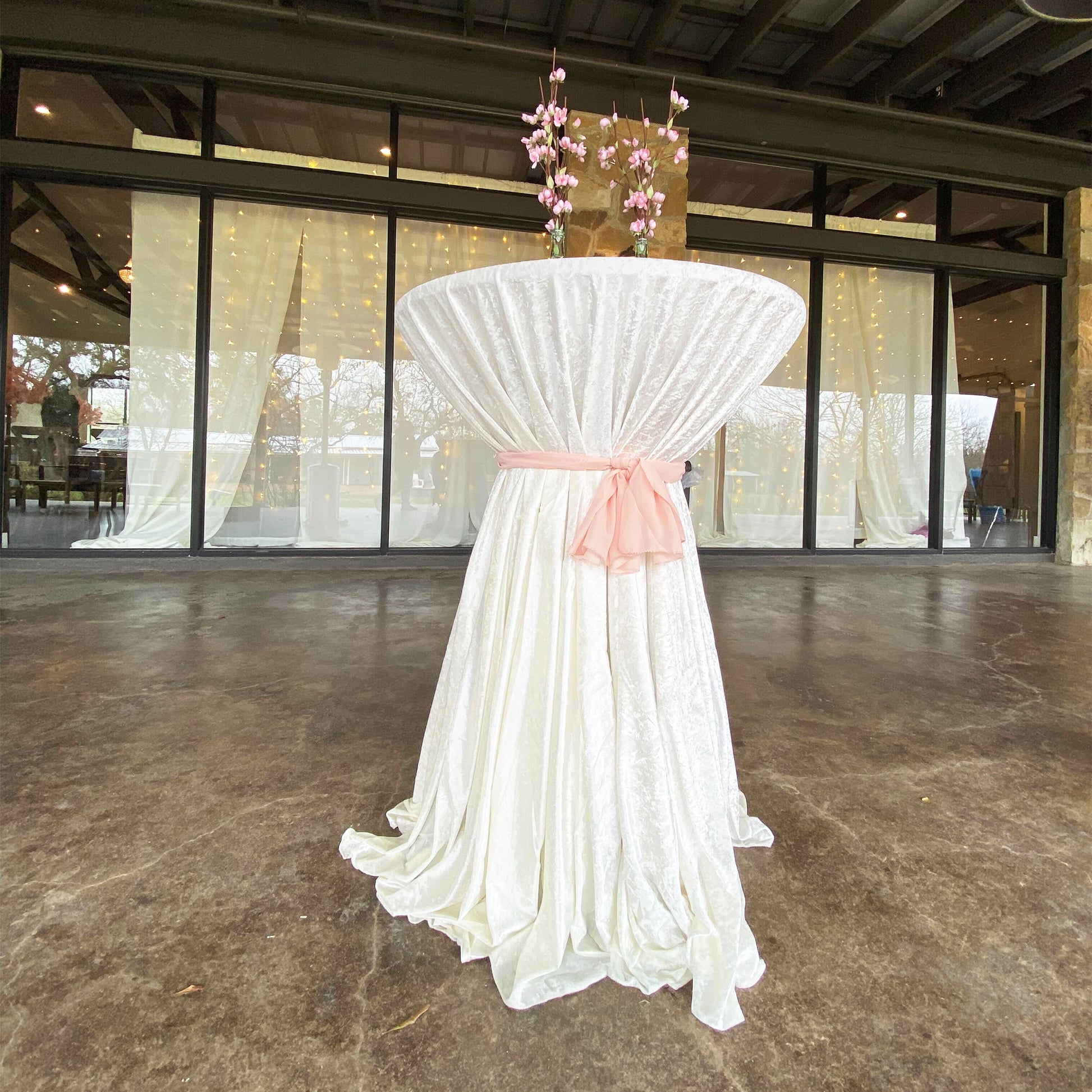Velvet 108" Round Tablecloth Ivory on a cocktail table with a lamour blush/rose gold sash tie