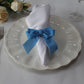Velvet Bow Tie Napkin Ring Baby Blue with a white napkin on top of an ivory charger plate
