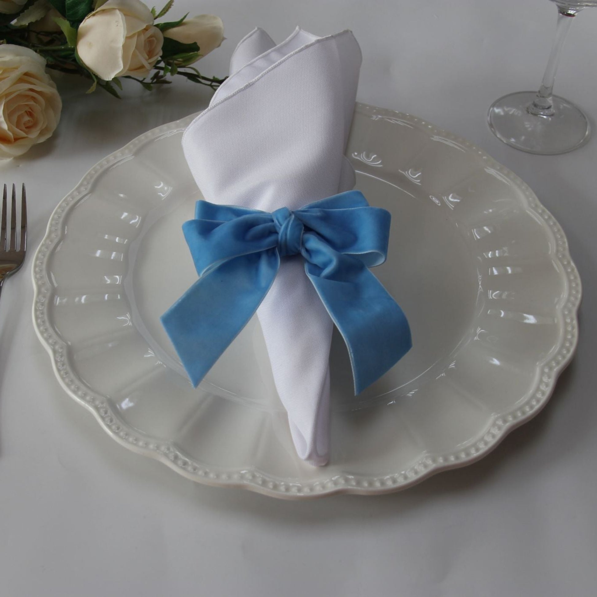 Velvet Bow Tie Napkin Ring Baby Blue with a white napkin on top of an ivory charger plate