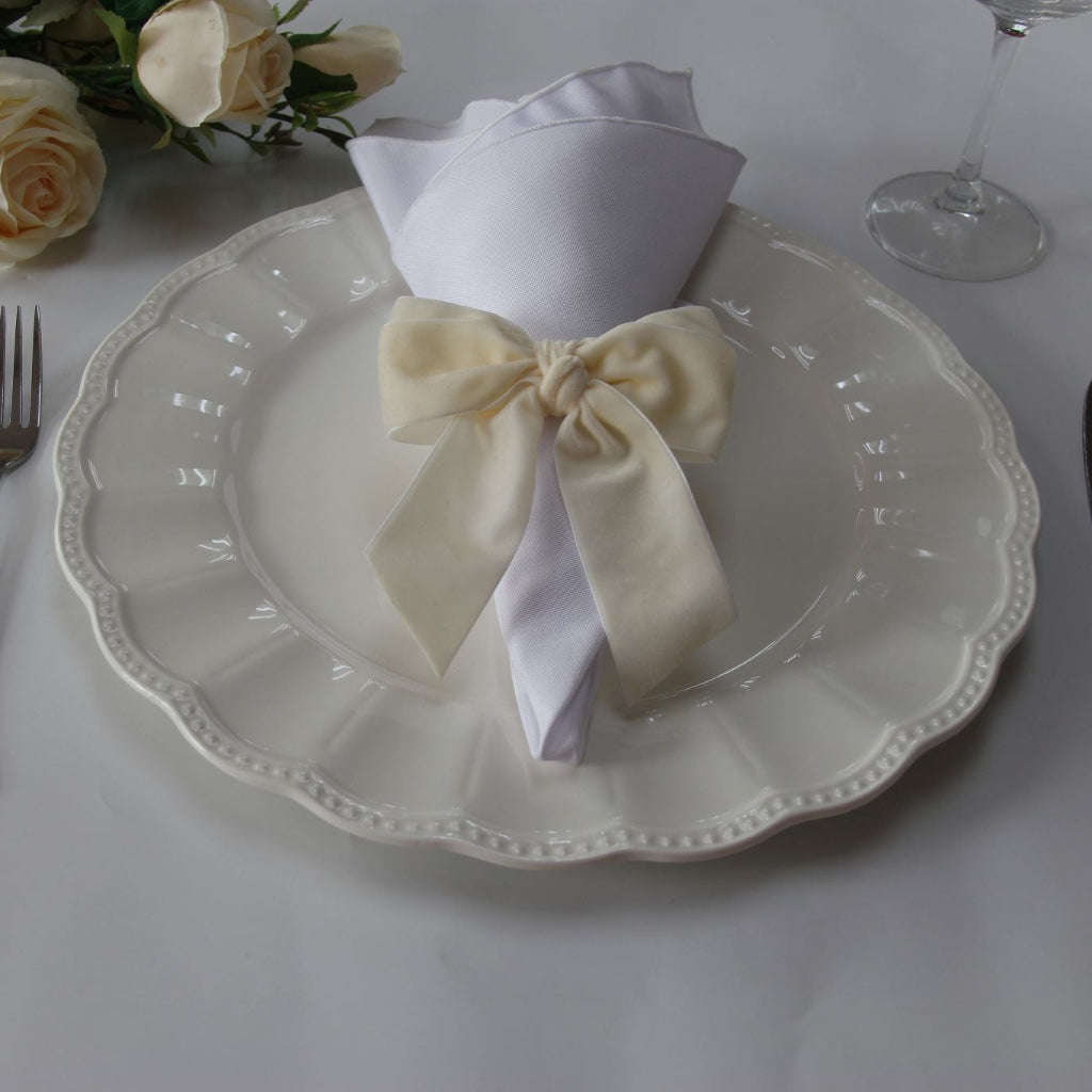 Velvet Bow Tie Napkin Ring Ivory with a white napkin on top of an ivory charger plate
