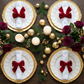 birdseye view of the Velvet Bow-Tie Napkin Ring Red on a white napkin on top a white dinner plate  and gold charger plate