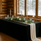 decorative tablescape of Velvet King 108"x156" Rectangular Tablecloth - Black setup with flowers, Christmas greenery, a cocktail glass, and tapered candles.