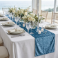 Velvet Table Runner Steele Blue on top a white polyester spun rectangular tablecloth, tapered candles, silver charger plates and dinner plates
