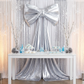 Giant metallic silver fabric bow backdrop over a white table with winter dessert spread, ideal for wedding reception decor