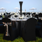 Outdoor table set up with black trumpet centerpiece, clear goblets, black tablecloth and chair covers