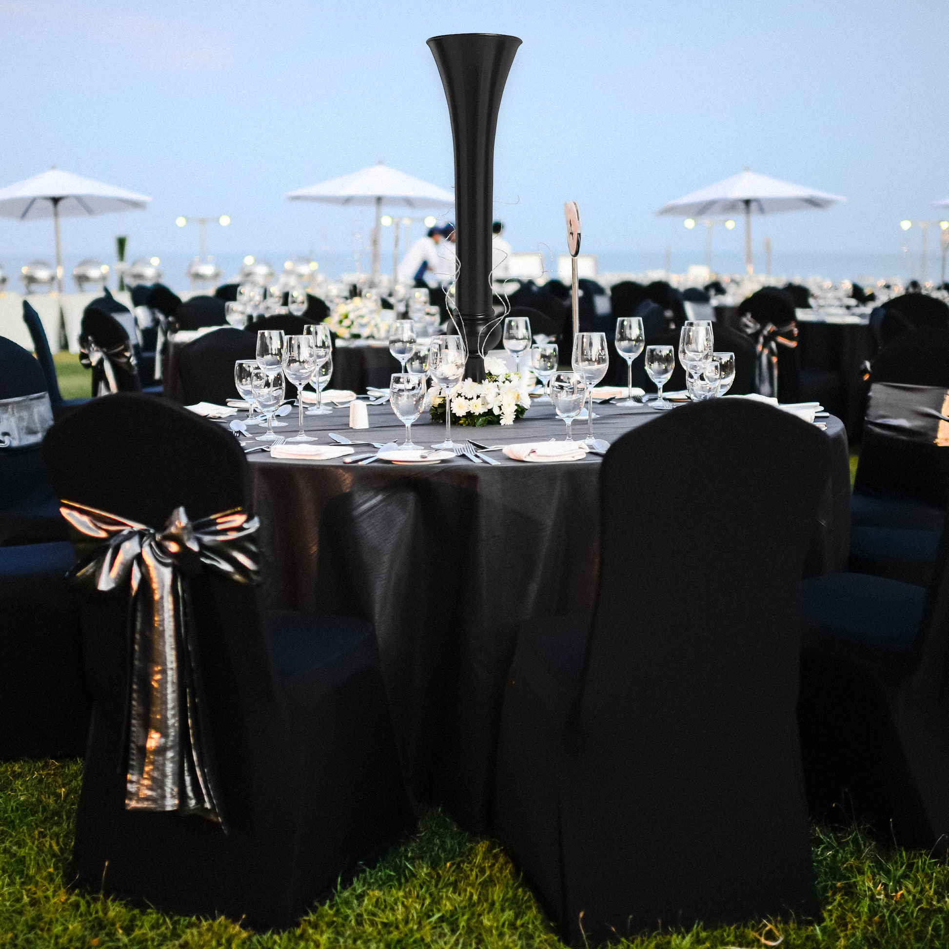 Outdoor table set up with black trumpet centerpiece, clear goblets, black tablecloth and chair covers