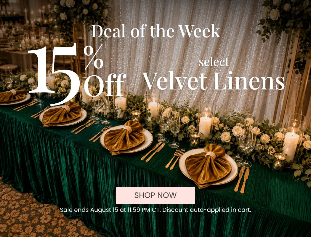 Lux velvet linens on a green banquet table for a wedding setup with candles and floral garlands.