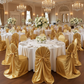 Elegant ballroom setup featuring white tablecloths and gold satin chair covers with self-ties for wedding receptions.