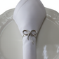 Silver rope bow tie napkin ring holding white linen napkin on white plate