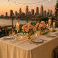 Decorative city view tablescape of ivory velvet tablecloth setup with flowers, dinnerware, a cocktail glass, and pillar candles.