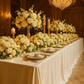 Decorative ballroom tablescape of ivory velvet tablecloth setup with white flowers, dinnerware, a cocktail glass, pillar candles and tapered candles